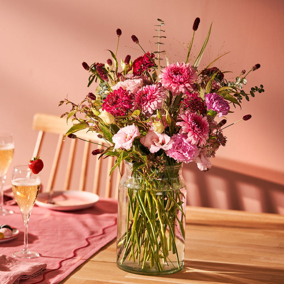 Sfeerfoto van een rond boeket met roze bloemen op een gedekte tafel